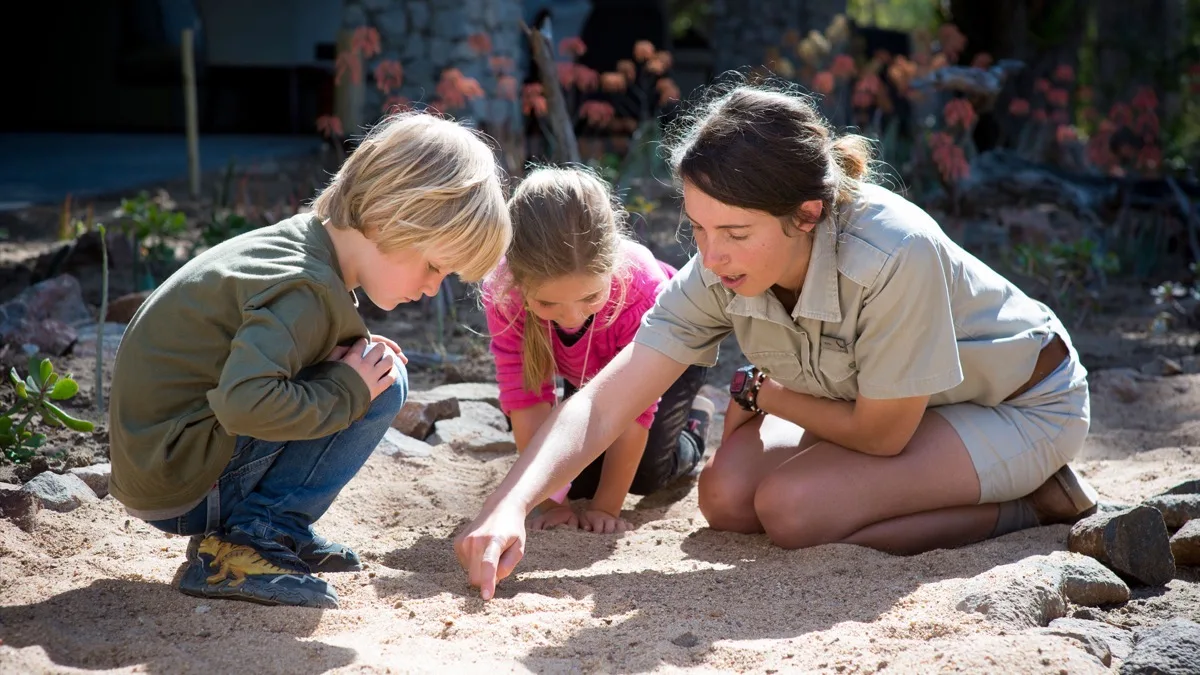Guide showing children animal tracks in the sand, family safari South Africa